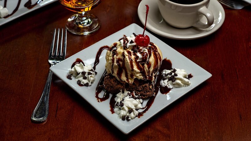 Brownie dessert topped with vanilla ice cream, chocolate syrup and whipped cream